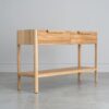 Tento odkládací stolek z masivního dubu kombinuje funkčnost s elegantním designem. Má dvě praktické zásuvky s charakteristickým drážkovaným čelem a minimalistickými úchyty, které dodávají moderní vzhled.