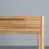 Tento odkládací stolek z masivního dubu kombinuje funkčnost s elegantním designem. Má dvě praktické zásuvky s charakteristickým drážkovaným čelem a minimalistickými úchyty, které dodávají moderní vzhled.