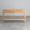 Tento odkládací stolek z masivního dubu kombinuje funkčnost s elegantním designem. Má dvě praktické zásuvky s charakteristickým drážkovaným čelem a minimalistickými úchyty, které dodávají moderní vzhled.